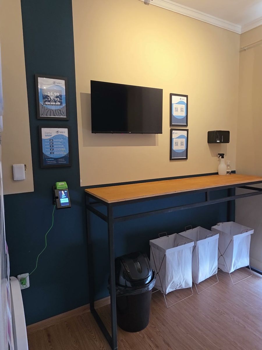 Bancada de dobrar com os cestos de tecido, a TV e os quadros com o passo a passo e os preços