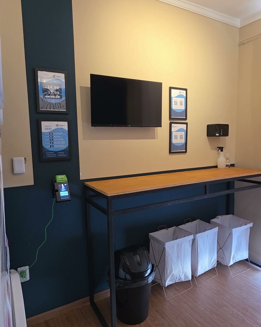 A bancada de dobrar roupa com TV, cestos e os pôsteres com QR code