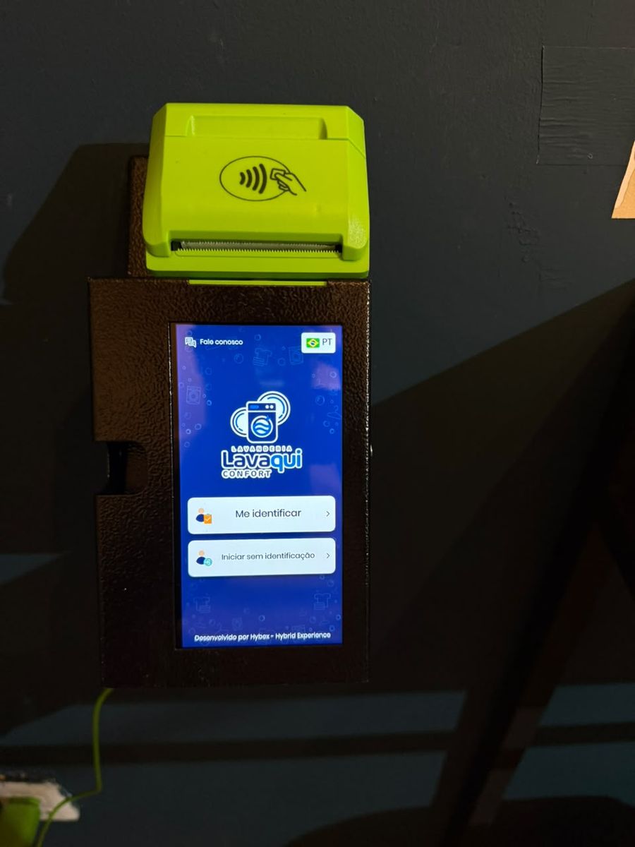 O totem de pagamento na parede, com a tela da Lavaqui e o leitor de cartão por aproximação